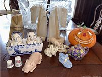 Photo showing all items on table: Delft Blue piggy salt and pepper set, three stone horse head bookends, two ceramic thimbles, ceramic teapot ornament, pig figurines, glass pumpkin
