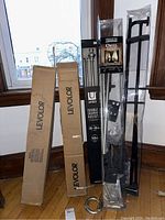 Full lot of three metal drapery rods and two boxed Levelor blinds, set against window background in room corner.