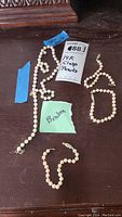 Pearl necklace and three bracelets on dark wood surface, tags visible including 'Broken' and '14K clasp Pearls'. Necklace and one bracelet broken, two bracelets wearable.