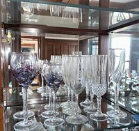 Shelved display of Lenox glassware including tall clear crystal champagne flutes with etched linear and diamond cut designs, and decorative purple swirl wine glasses.