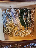 Overview of all necklaces in drawer showing various styles and colors including faux pearls, gold-tone beads, silver chain, and green bead strands.