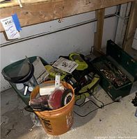 Photo showing bucket with Skil Saw power tool, cords, and accessories, and green toolbox on concrete floor.