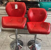 Photo showing front view of two red adjustable bar stools with metal bases on tiled floor.