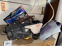 Skil and Black & Decker belt sanders along with boxed Ryobi dust shroud and other tools on wooden surface.