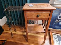 Shows the metal two-shelf stand and the wooden side table with drawer side by side on floor, visible wear and rust on metal shelf, wood has surface marks.