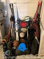 Photo showing stacked skis, ski poles, sports balls including volleyballs and basketballs, ski boots, and a sports bag in a basement setting.