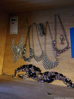 Seven sparkly rhinestone necklaces arranged on wooden surface including a notable purple neckpiece with matching earrings.