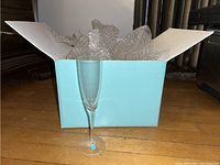 Single clear Tiffany & Co. champagne glass in front of an open Tiffany blue box with bubble wrap.