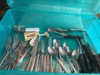Photo showing an assortment of forks, knives, spoons, and kitchen tools in a blue plastic container.