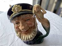 Close-up view of the ceramic stein showing the detailed face of the old sailor and the mermaid handle in natural light.