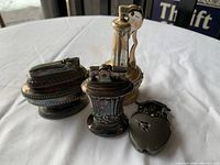 Four vintage novelty lighters arranged on a white cloth, showing varied shapes and styles including heart-shaped, blowtorch-style, and ornate bodies.