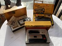 Three vintage Kodak cameras in original boxes with accessories and film inside.