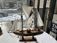 Full view of the wooden model sailboat with white sails displayed on a table with window background showing snowy street.