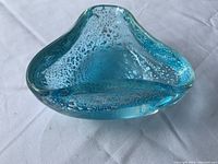 Top and angled view of a blue Murano glass bowl with silver flecks visible inside the glass, placed on a white fabric surface.