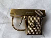 Top side view of the miniature gold-tone pistol lighter showing 'Legend' mark and textured grip with emblem