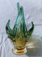 Front view of a multicolored Murano glass basket showing the folded handle design and the sunlit color gradients from amber at the base to green at the top.
