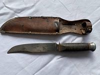 Photo showing full view of vintage fixed blade knife with its leather sheath, highlighting the blade, handle, and sheath details.