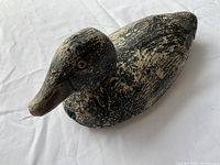 Angled close-up view of vintage wooden duck decoy highlighting glass eye and worn paint surface.