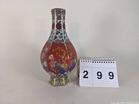 Front view of the porcelain hexagonal vase with a red base, showing floral and bird motifs and an numbered tag '299'.