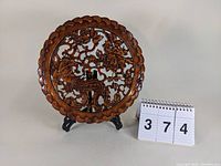 Front view of the round carved wood plaque depicting a pheasant and floral design on a stand.