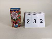 Side view of the same cloisonné-style vase next to a notebook with numbers for lot identification and scale reference.