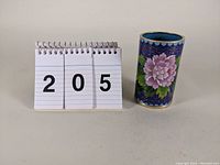 Photo showing the 4 inch tall cloisonne cylindrical vase with a floral design next to a size reference.