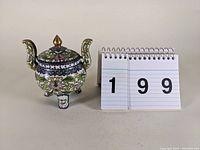 Full view of the 4 inch cloisonne double handled jar next to a flip calendar for scale.
