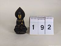Front view of the brass/bronze Buddha statue next to number cards showing '192' for lot identification.