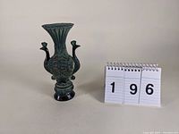 Angle view of bronze vase with double peacock and flared top beside numbered card