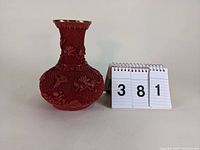 Front and side view of red cinnabar-style vase with raised floral and butterfly decorations and gold rim