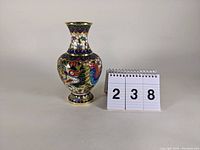 Front angle view of the cloisonne-style vase with dragon and floral enameled design, standing next to a number placard.