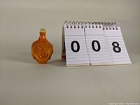 Photo of amber colored snuff bottle with pheasant and dragon carving and numbered lot display