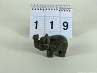 Front angled close-up view of green and brown stone elephant figurine with carved spiral designs, showing trunk raised and details on ears.