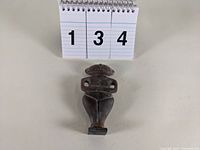 Front view of carved hard stone fetish figure on neutral white background with numeric card in background