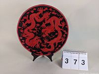Front view of the 11 1/8 inch cinnabar-style decorative charger plate on stand with red dragon design on a black background.