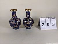 Pair of deep blue cloisonné vases with floral and branch designs shown alongside table number 203.