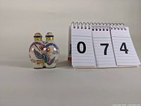Front view of the conjoined porcelain double snuff bottle placed next to number cards for scale, showing colorful bird and floral decoration.