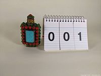 Front and angled view of the small rectangular snuff bottle showing turquoise-colored central jewel, surrounded by coral and green jewels with metal ornate setting and a jeweled stopper.