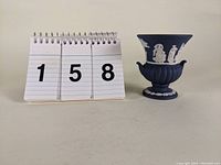 Dark blue Jasperware urn vase next to number sign showing height scale