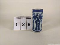 Front view of the Wedgwood cylindrical jasperware vase showing white classical relief on dark blue background with size reference.