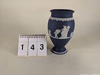 Front view of the dark blue jasperware urn vase with white classical relief decorations including a woman and cherubs.