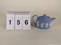 Overall view of the small 3-inch Wedgwood light blue jasperware teapot next to number cards showing lot 156