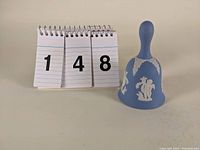 Front angled view of the blue Wedgwood jasperware bell with white classical relief beside numbered display.
