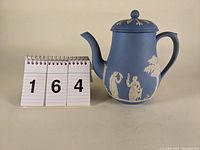 Light blue Wedgwood jasperware coffee pot positioned next to numbered stand showing size and lot number.