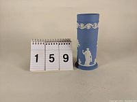 Front view of the Wedgwood light blue Jasperware cylindrical vase showing classical white relief figures and decorative band near top.