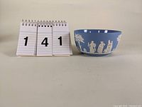 Front view of the light blue bowl showing white classical figures and trees in raised relief.