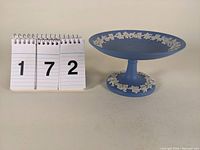 Front side view showing the light blue tazza with white grapevine relief decoration on base and rim, alongside the lot number