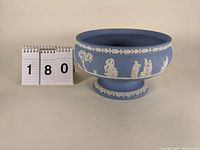 Front and side view of the 8 inch light blue Wedgwood jasperware footed bowl showing white classical figures and decorative reliefs.