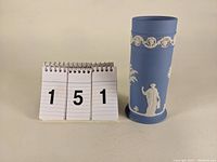 Light blue Wedgwood jasperware cylinder vase with white classical relief decoration, showing front and details.