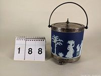 Front view of the blue Wedgwood jasperware biscuit jar with silverplate mounted lid and handle, showing white classical figures in relief.